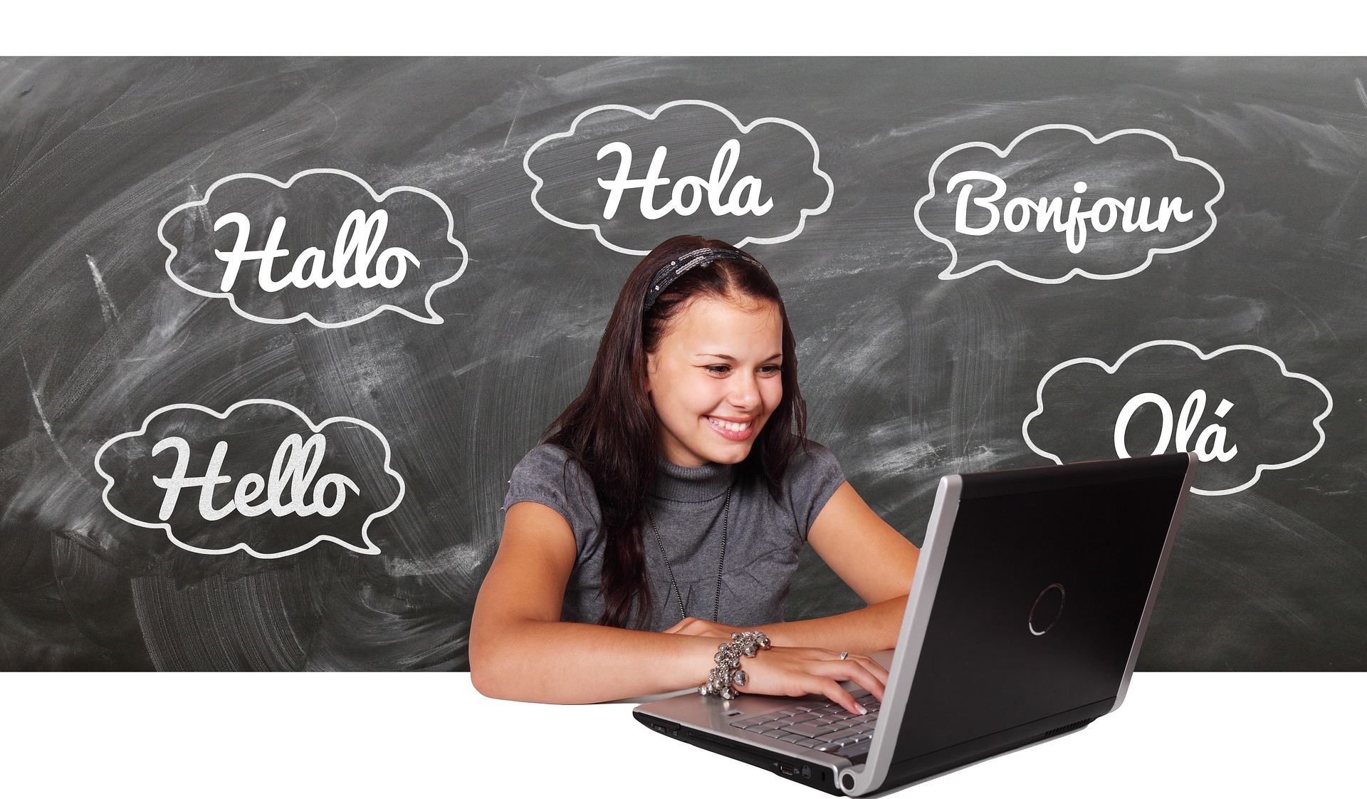 A woman sits at a laptop in front of a chalkboard that has "hello" writing in several languages